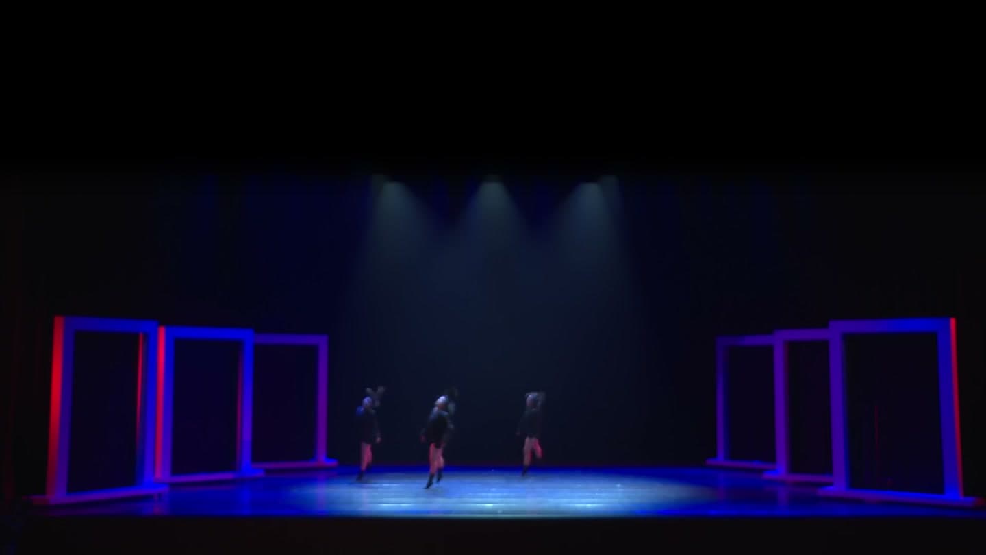 Three performers on a dark stage framed by blue and red-lit rectangular door frames.